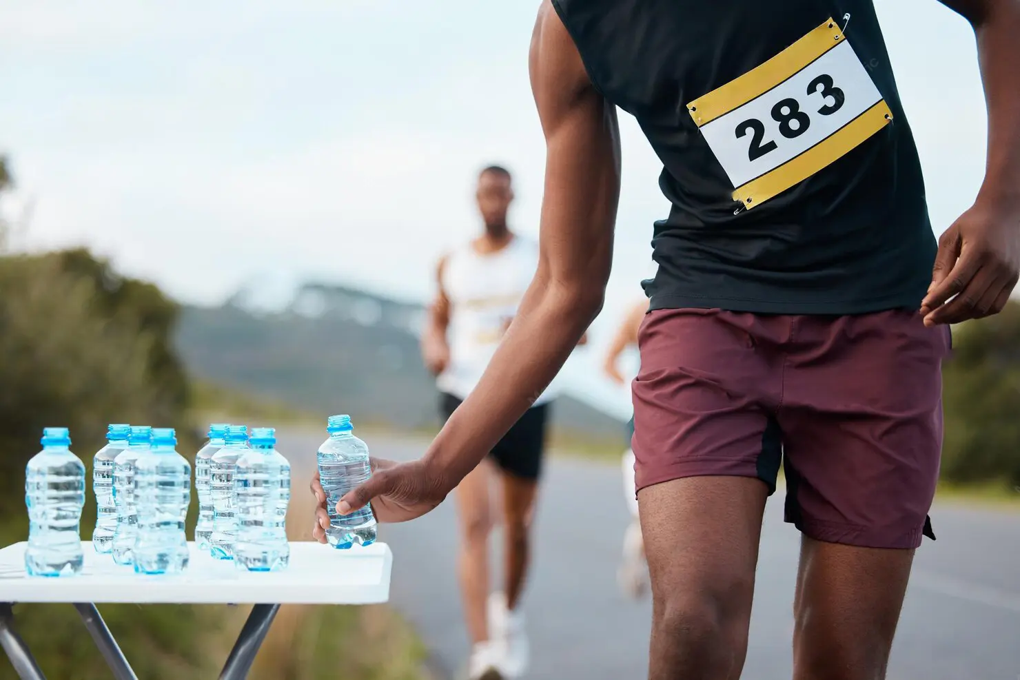 A volunteer hands a runner a bottle of water at a hydration zone along The Circuit course